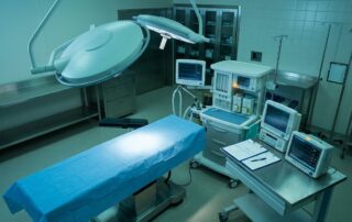 An empty surgical bed and anesthesia equipment under soft clinical lighting in an operating room.
