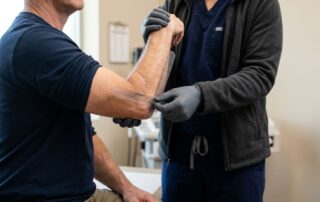 A medical professional measures a patient's elbow flexion with a goniometer.