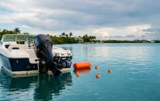 Damaged boat with a raised propeller, orange buoy, and evidence markers on calm coastal water.