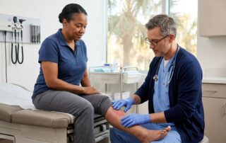 A doctor examines a patient’s swollen, reddened lower leg in a hospital room.
