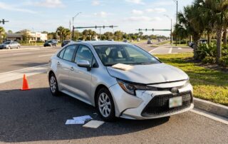 Damaged rental sedan parked near a Florida intersection with an orange cone and claim documents.