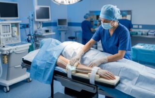 Clinician checks padded arm supports beside a draped patient in an operating room.