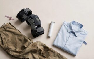 A knee brace, medication tube, stained trousers, and folded shirt arranged on a neutral background.